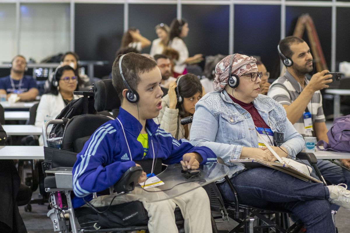 Jovem com deficiência usando fones de ouvido para acompanhar a palestra no congresso Reatech. Ele está em uma cadeira de rodas com tecnologia assistiva.