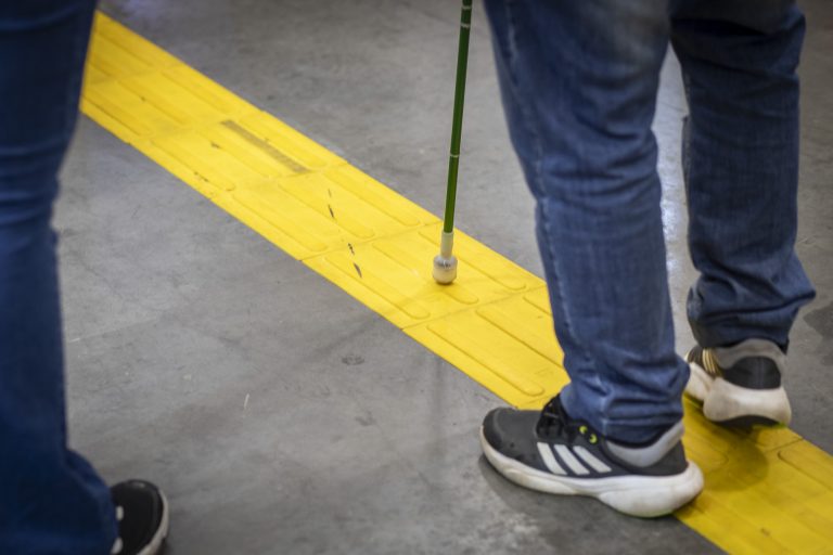 Pessoa com deficiência visual utilizando piso tátil de acessibilidade em evento inclusivo