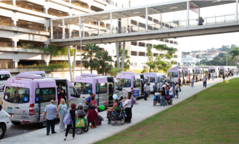 Vans de transporte acessível em fila para embarcar pessoas, incluindo cadeirantes.