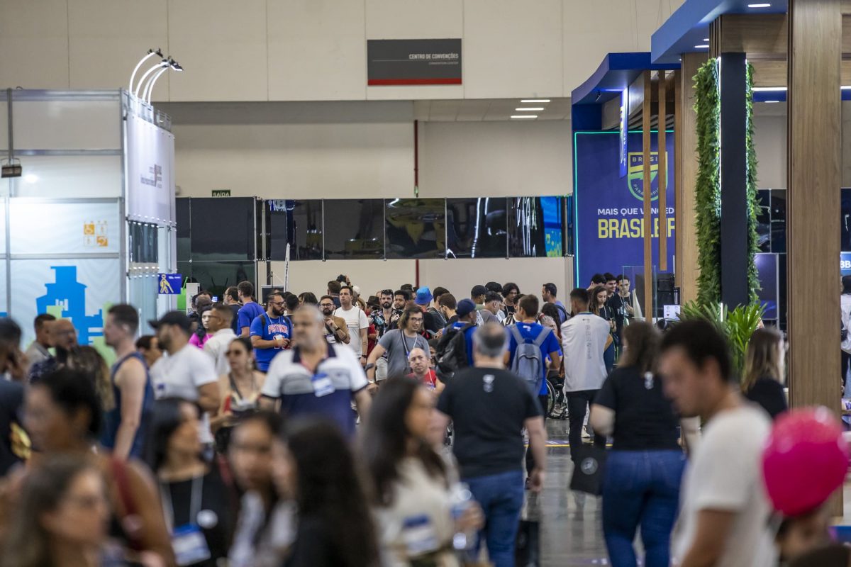 Grande fluxo de pessoas no corredor principal do congresso Reatech, com banners e estandes ao fundo.