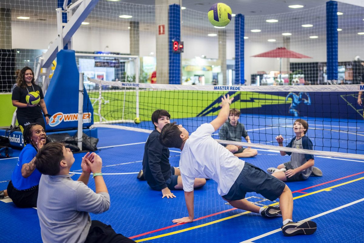 Grupo de participantes se diverte jogando vôlei sentado. Um deles atinge a bola com a mão.
