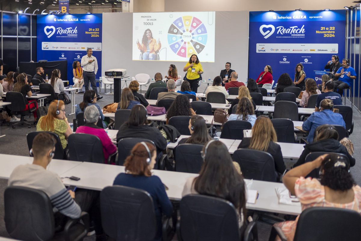 Visão geral de uma palestra no congresso Reatech, mostrando a plateia e os palestrantes no palco