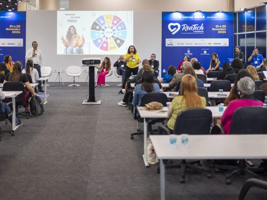 Visão geral de uma palestra no congresso Reatech, mostrando a plateia e os palestrantes no palco.