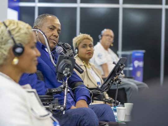 Público com e sem deficiência assiste a uma palestra sobre inclusão no congresso Reatech. Homem em cadeira de rodas no centro.